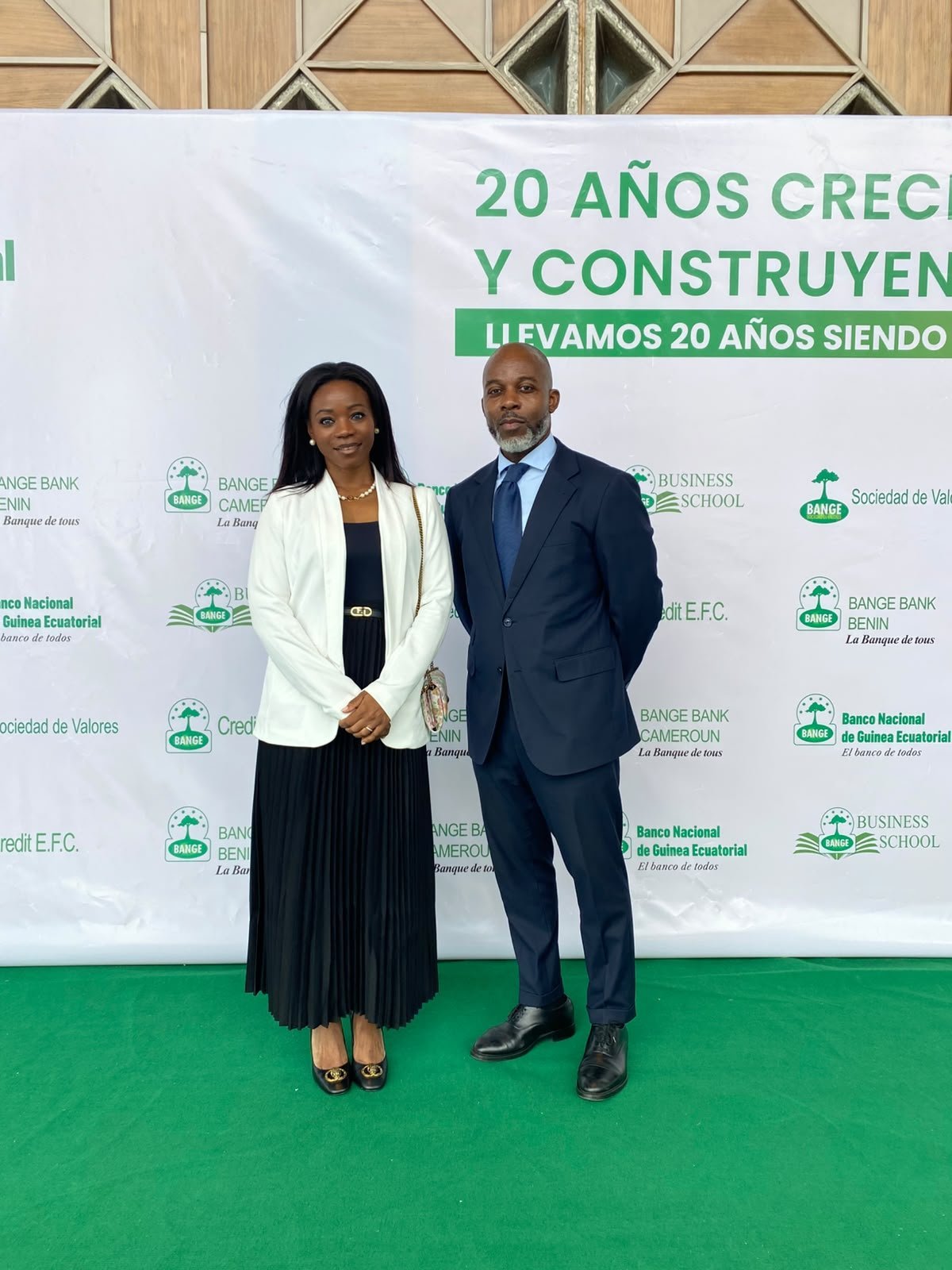 Two attendees pose for a full-length photograph in front of the backdrop for BANGE's 20th anniversary.
