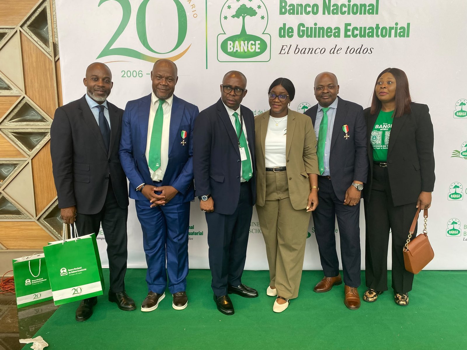 Six attendees pose in front of the Banco Nacional de Guinea Ecuatorial's 20th anniversary backdrop.