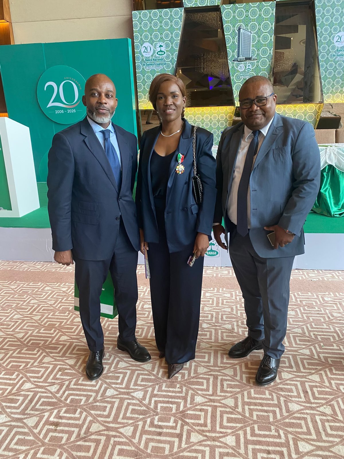 Three attendees pose beside the stage decorated for BANGE's 20th anniversary.